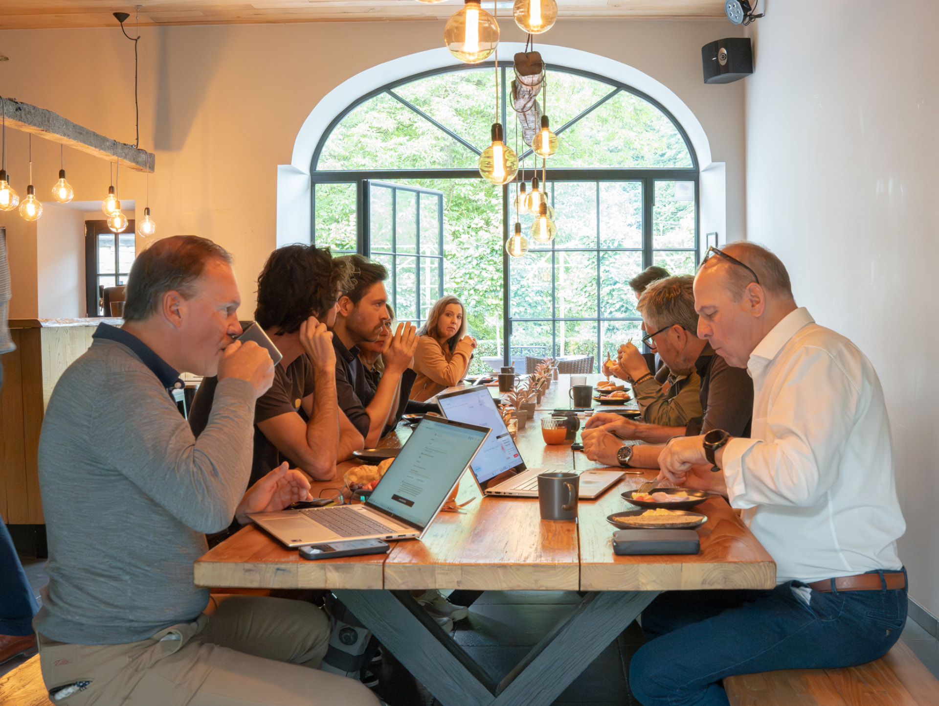 Deelnemers werken samen op laptops aan een lange houten tafel