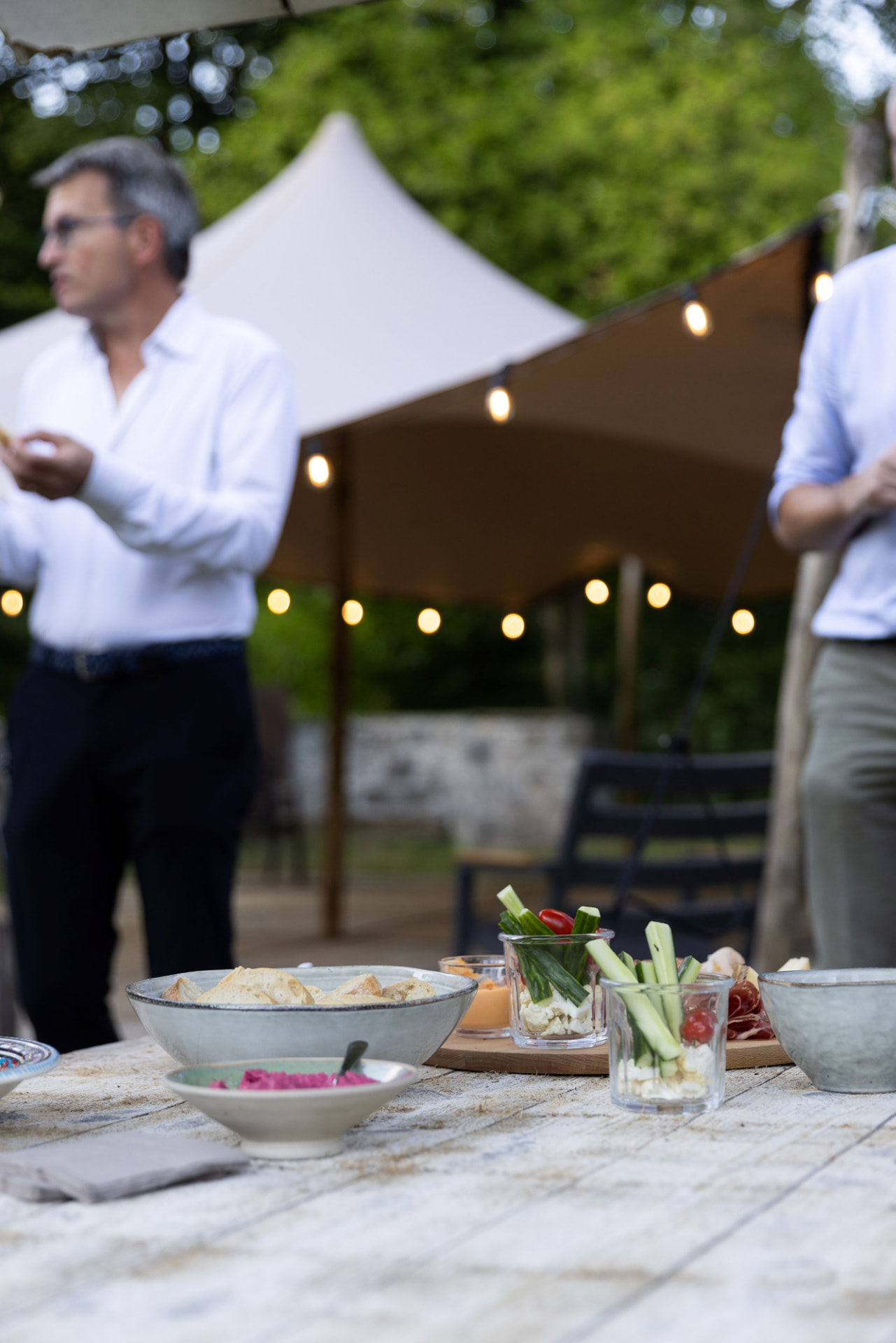 Een gastheer spreekt gasten toe onder de tent met lichtjes